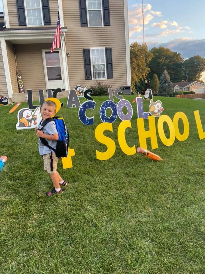 A young boy is standing in front of a sign that says school.  Back to school themed yard card.