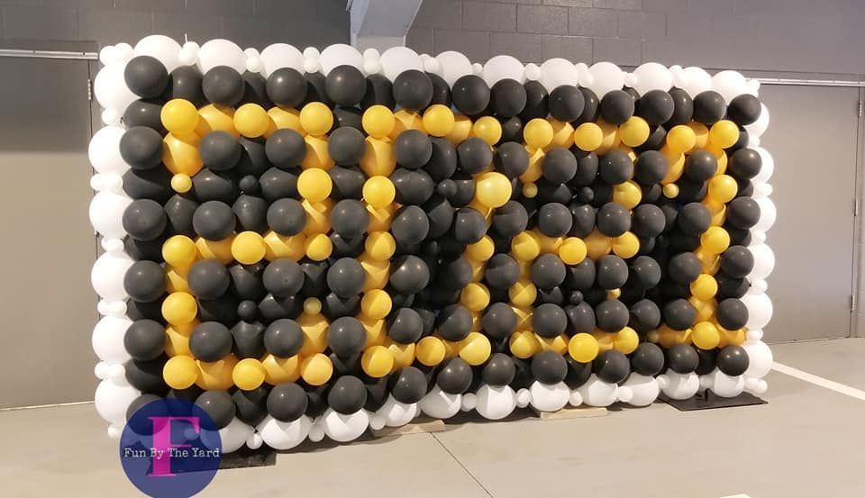 A wall made of black , yellow and white balloons.