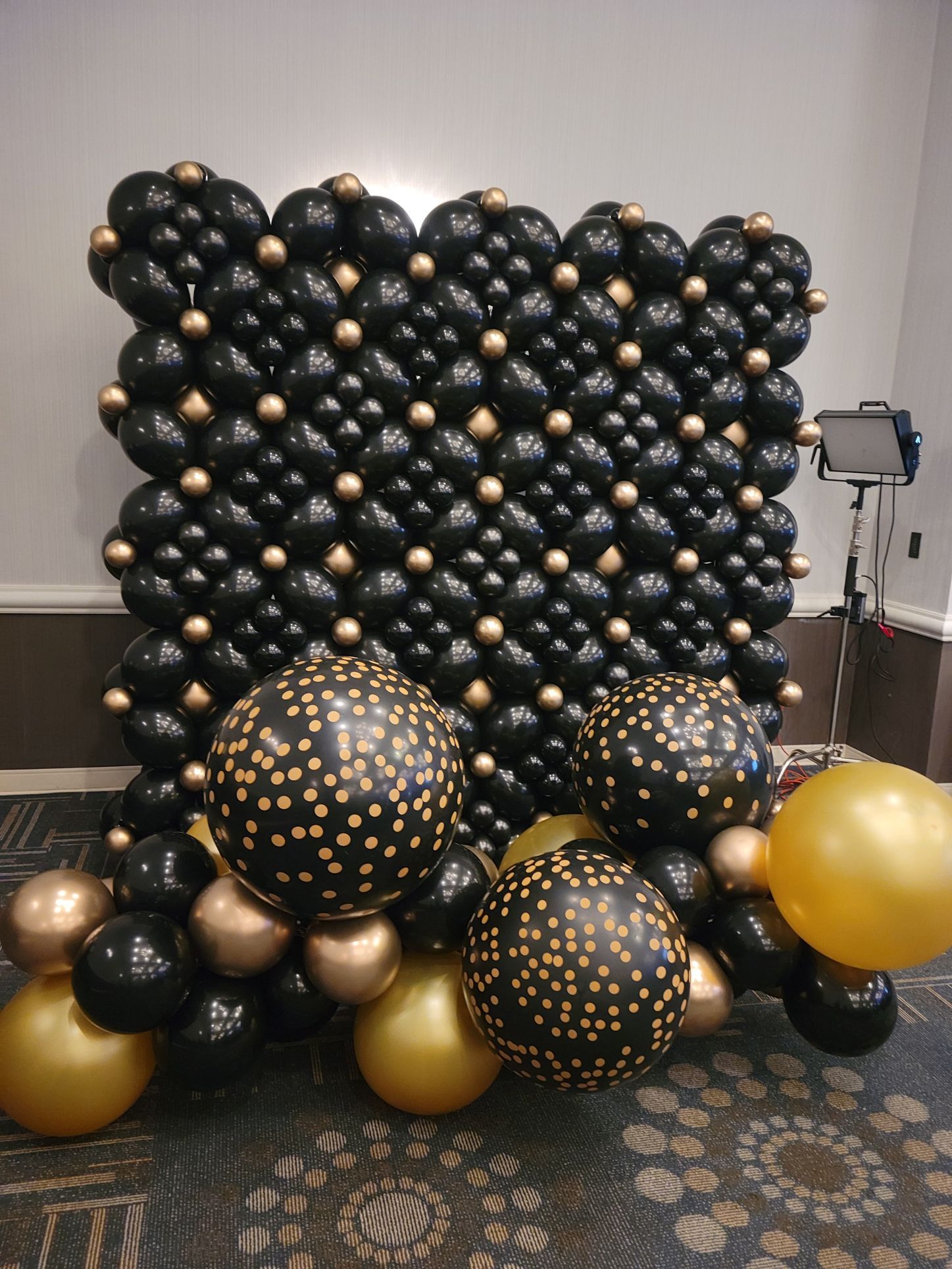 A wall made of black and gold balloons in a room.