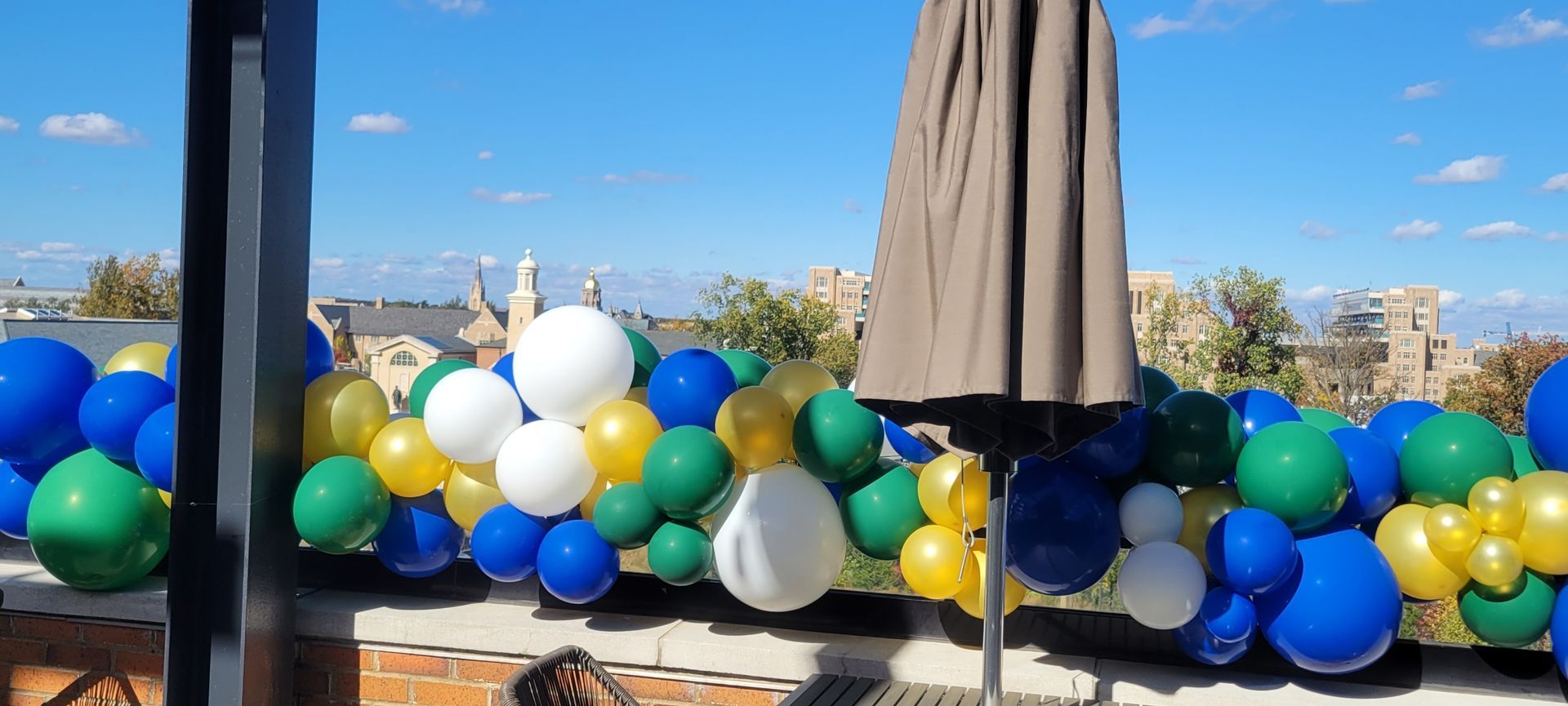 A sunny day with blue sky and balloons of white, yellow, green, and blue on a patio.