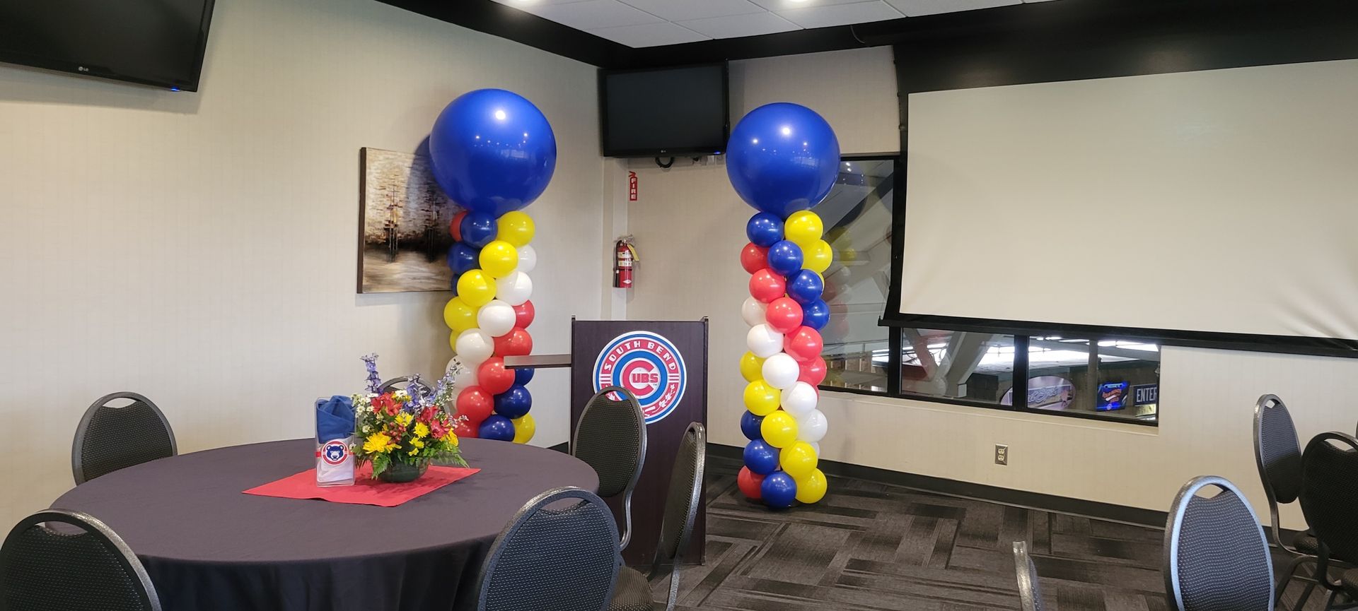 A room with tables and chairs and balloon columns at South Bend Cubs