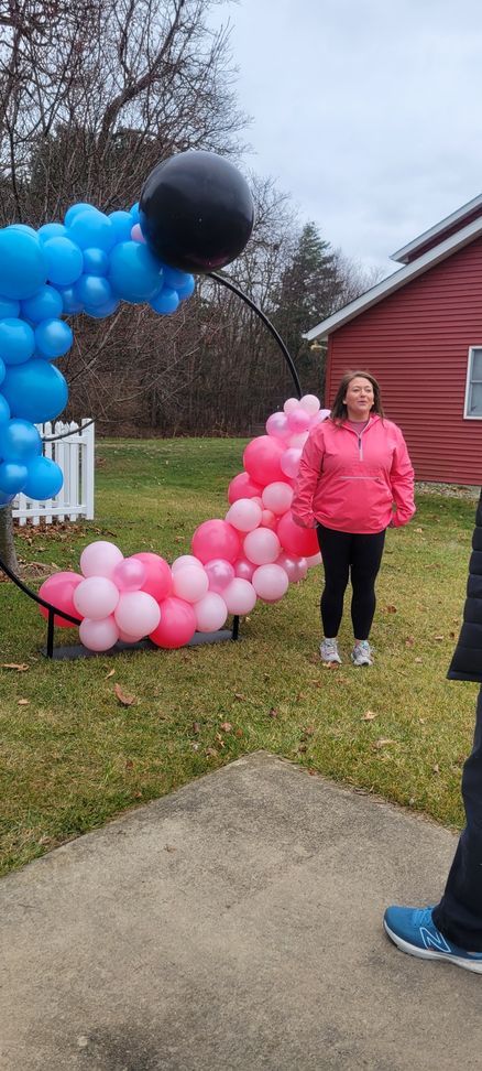 A woman is standing in front of a balloon photo op for a gender reveal.