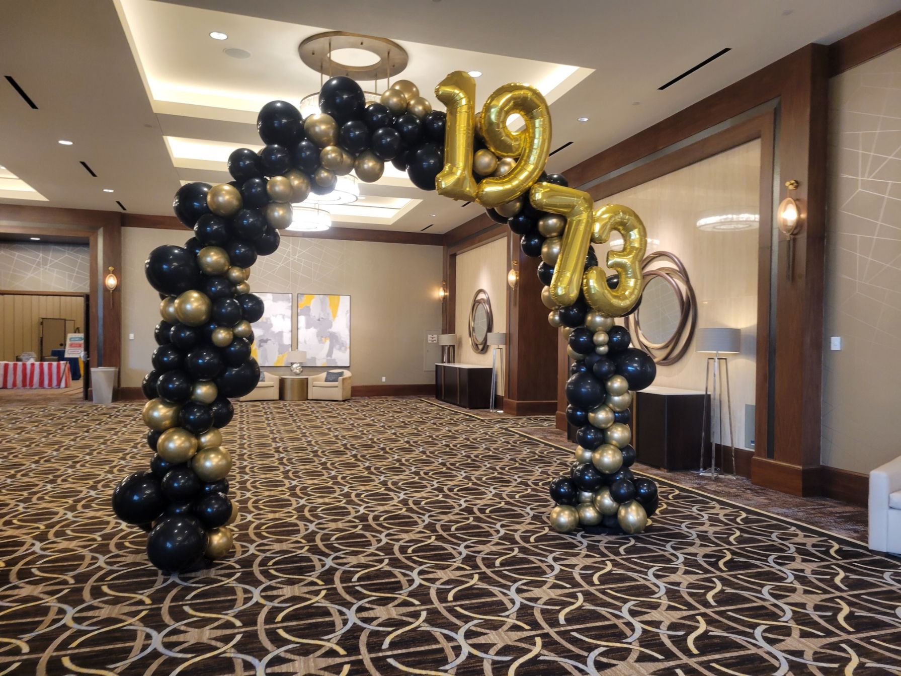 A large arch made of black and gold balloons in a room.