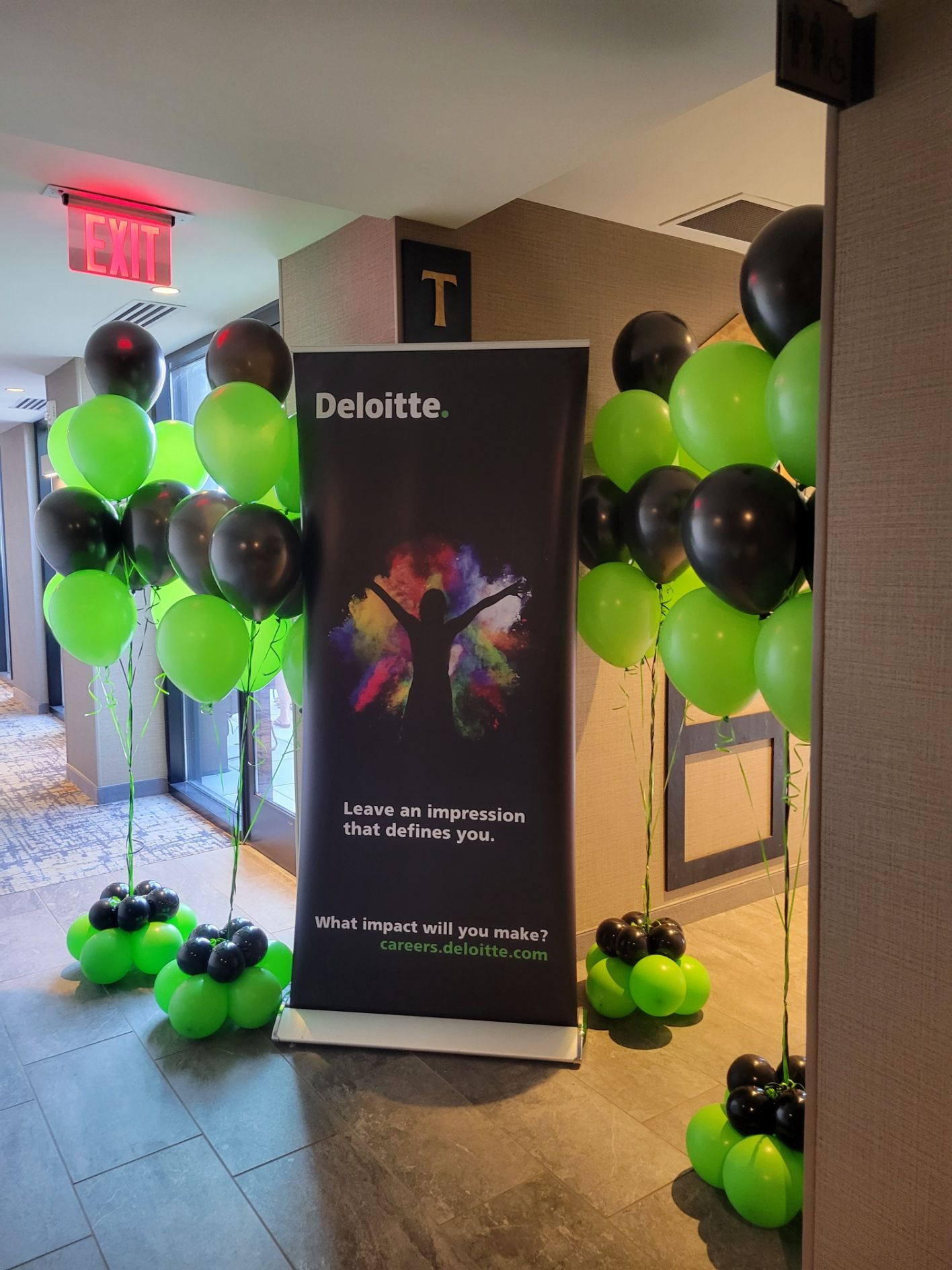 Deloitte banner flanked by black and green balloons, likely for an event in a hallway.