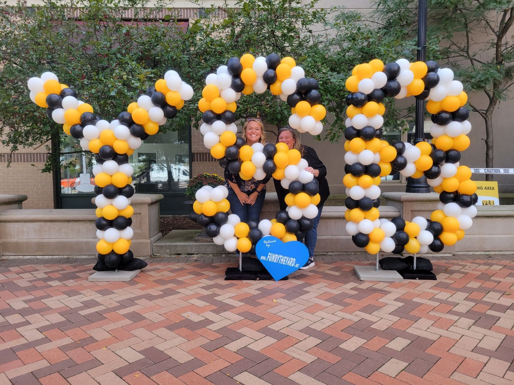 Two people are standing in front of a sign made of balloons that says YSB.