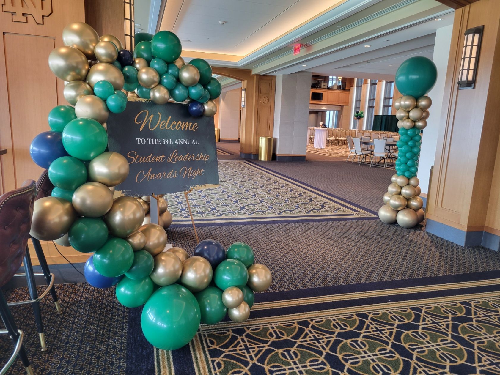 A room decorated with green and gold balloons and a welcome sign.