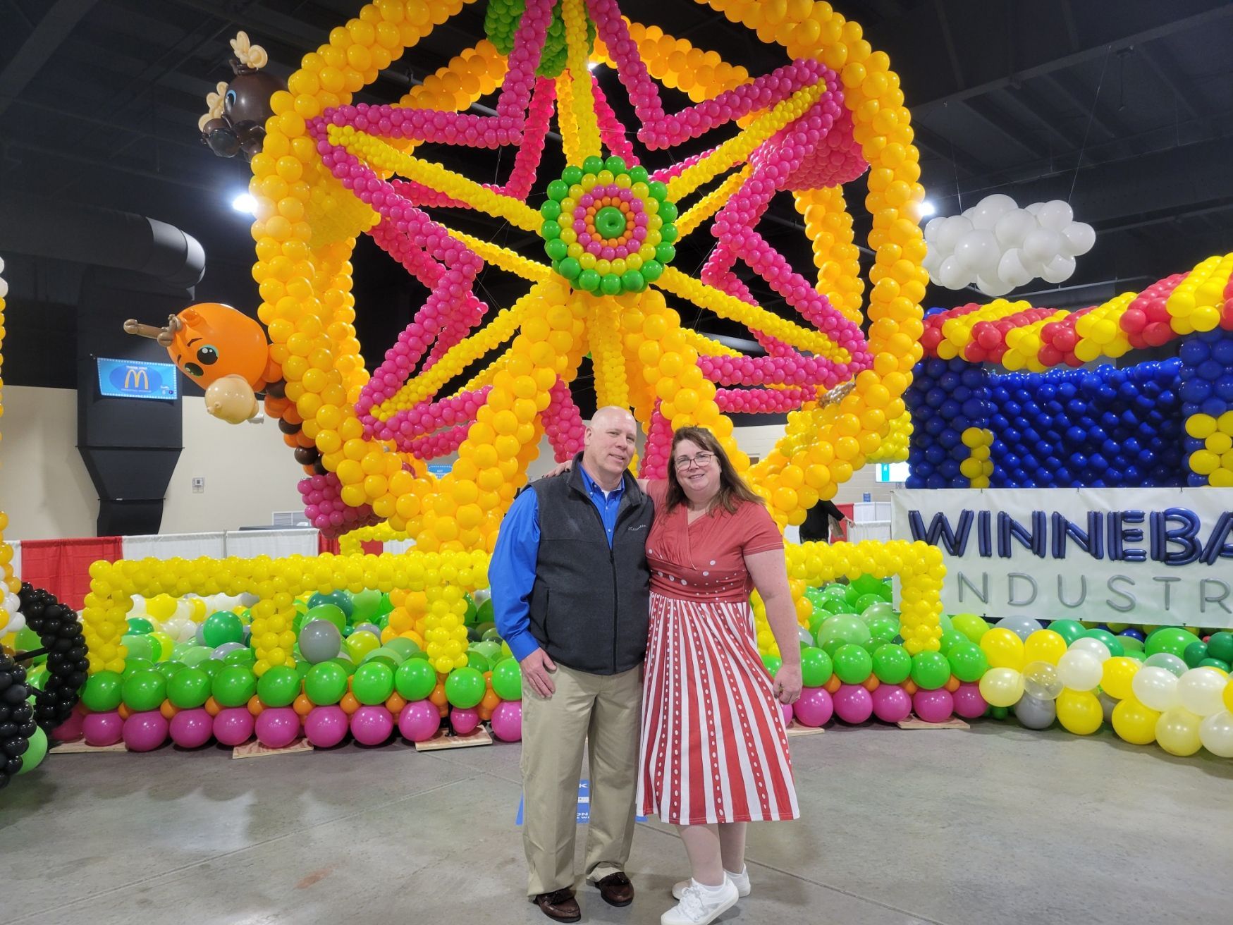 A man and woman are standing in front of a ferris wheel made of balloons  Fun By The Yard