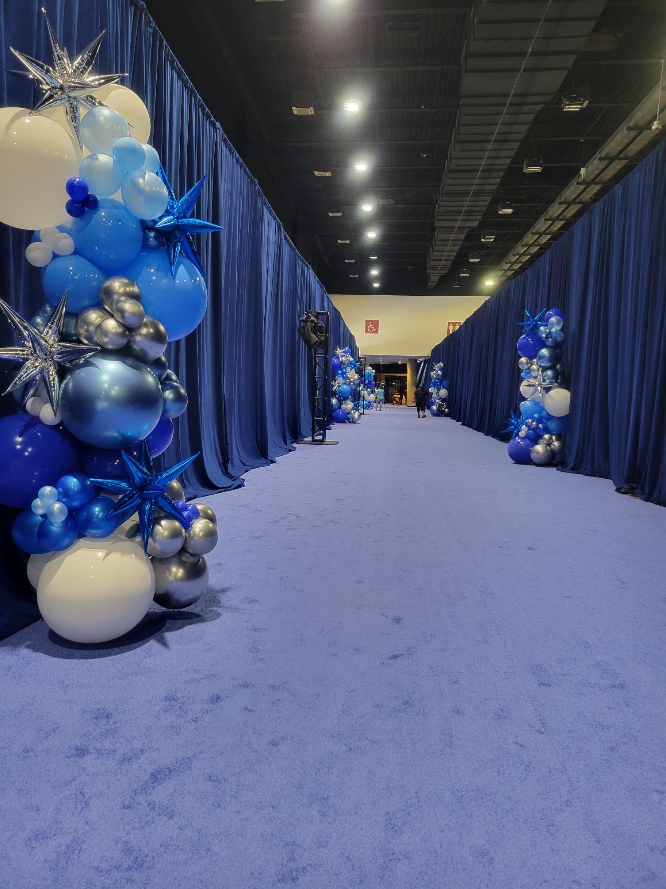 A hallway filled with blue and white balloons and blue curtains.
