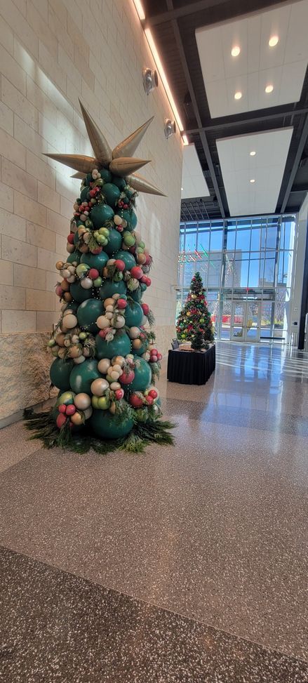 A christmas tree of balloons is sitting in the middle of a hallway in a building.