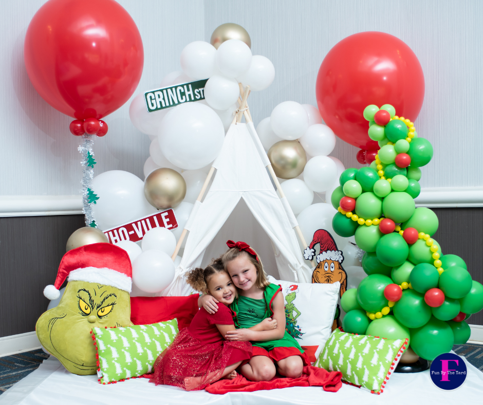 Two little girls are sitting in a teepee surrounded by balloons.