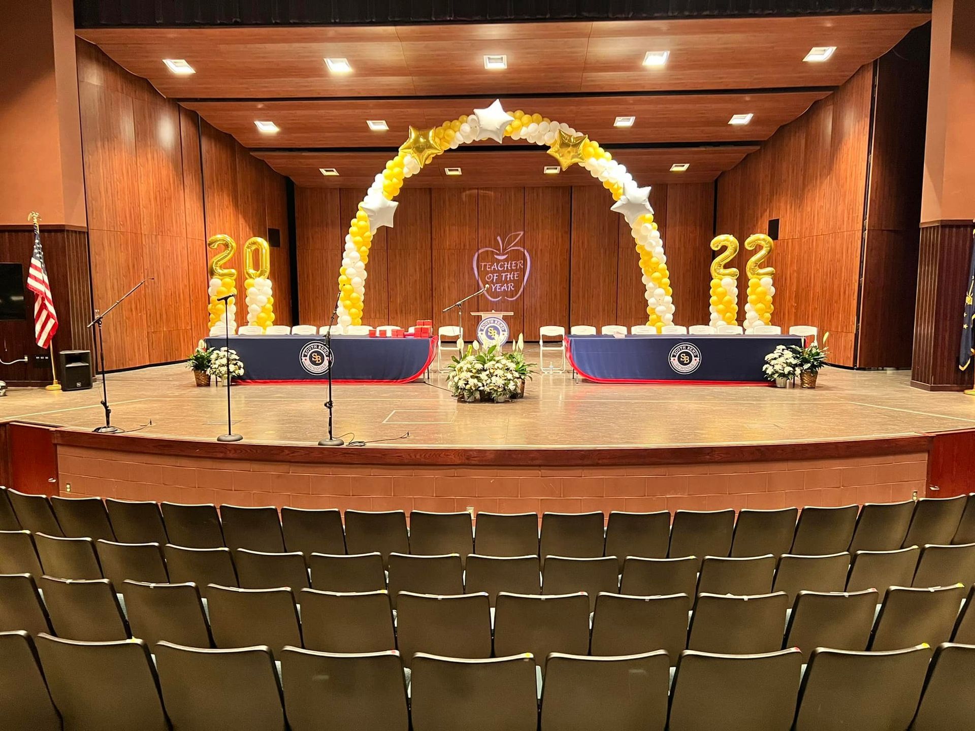 A large auditorium with a stage decorated for a graduation ceremony.