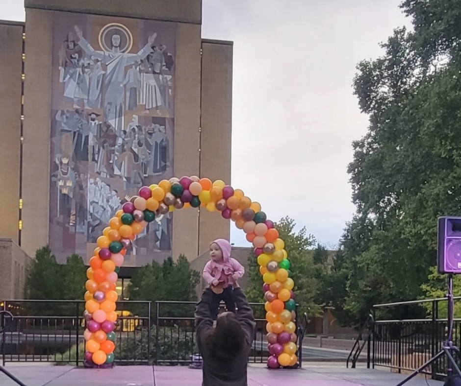 a person holding a baby under an arch of balloons