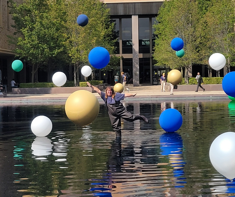 A woman is jumping in the water surrounded by balloons