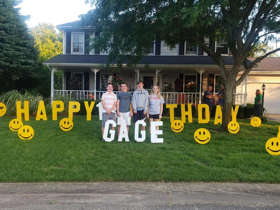 A group of people standing in front of a house with a sign that says happy birthday gage