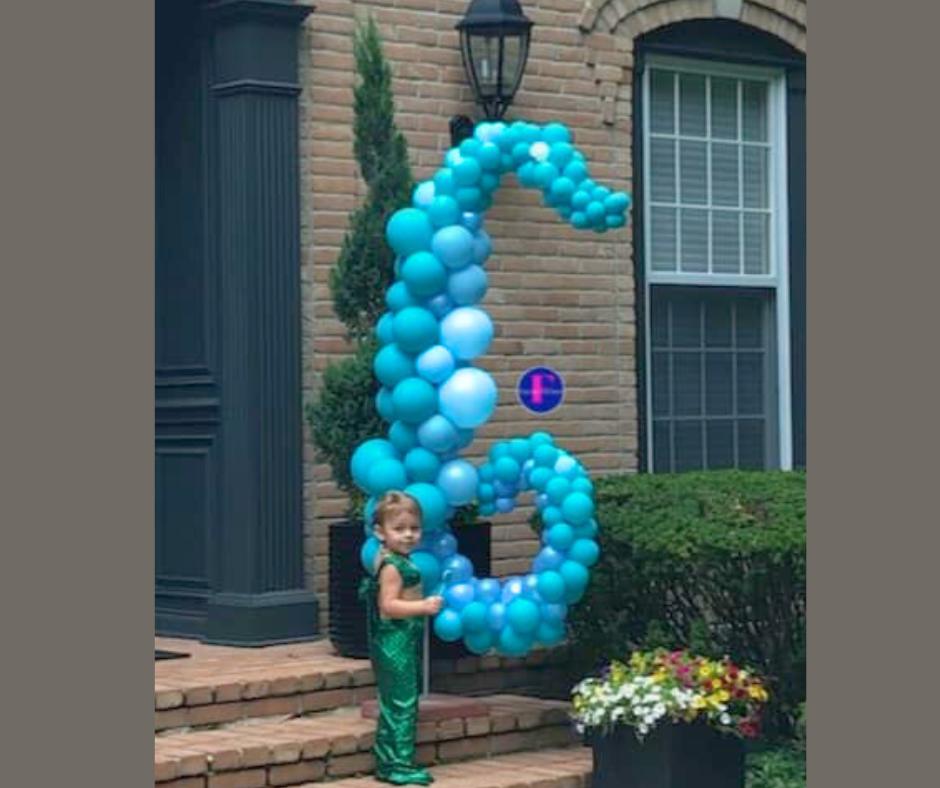 Girl in mermaid costume with blue balloon seahorse in front of a house.