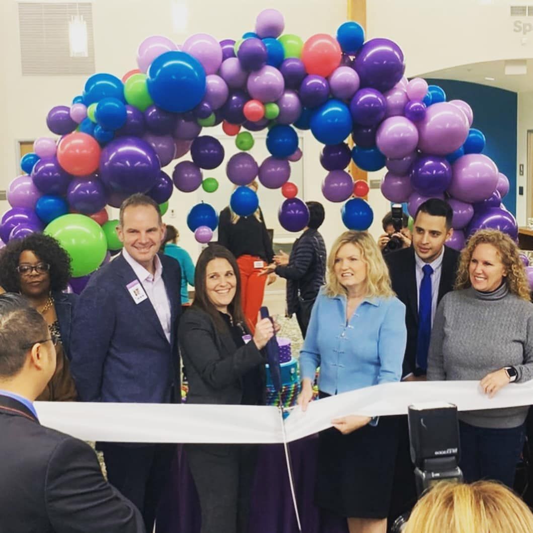 People cutting a ribbon under a balloon arch at an event.