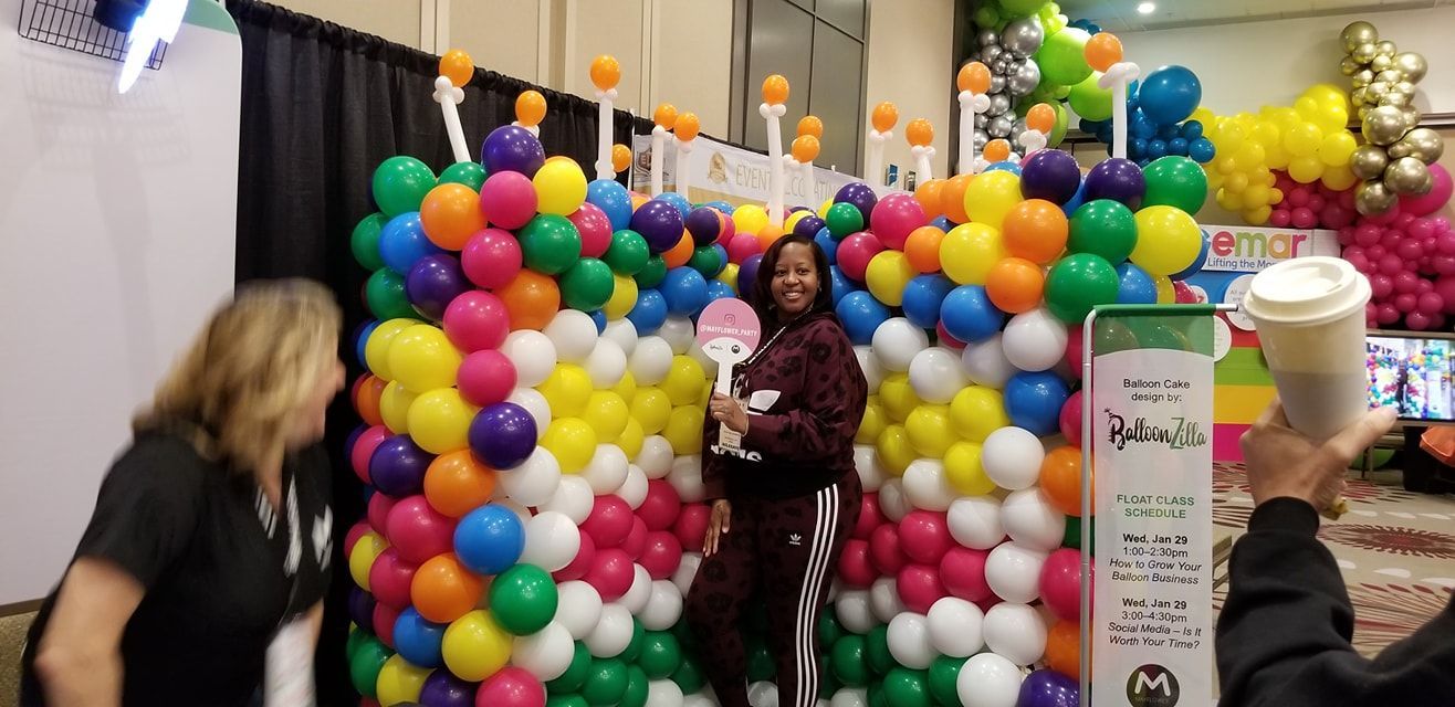 A woman is standing in front of a wall of balloons. Tradeshow balloons