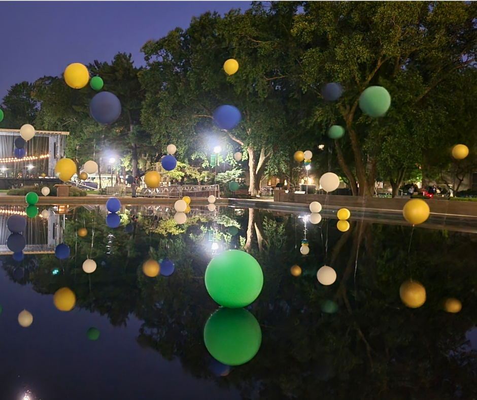 A bunch of balloons are floating in the water in the reflecting pool at Notre Dame