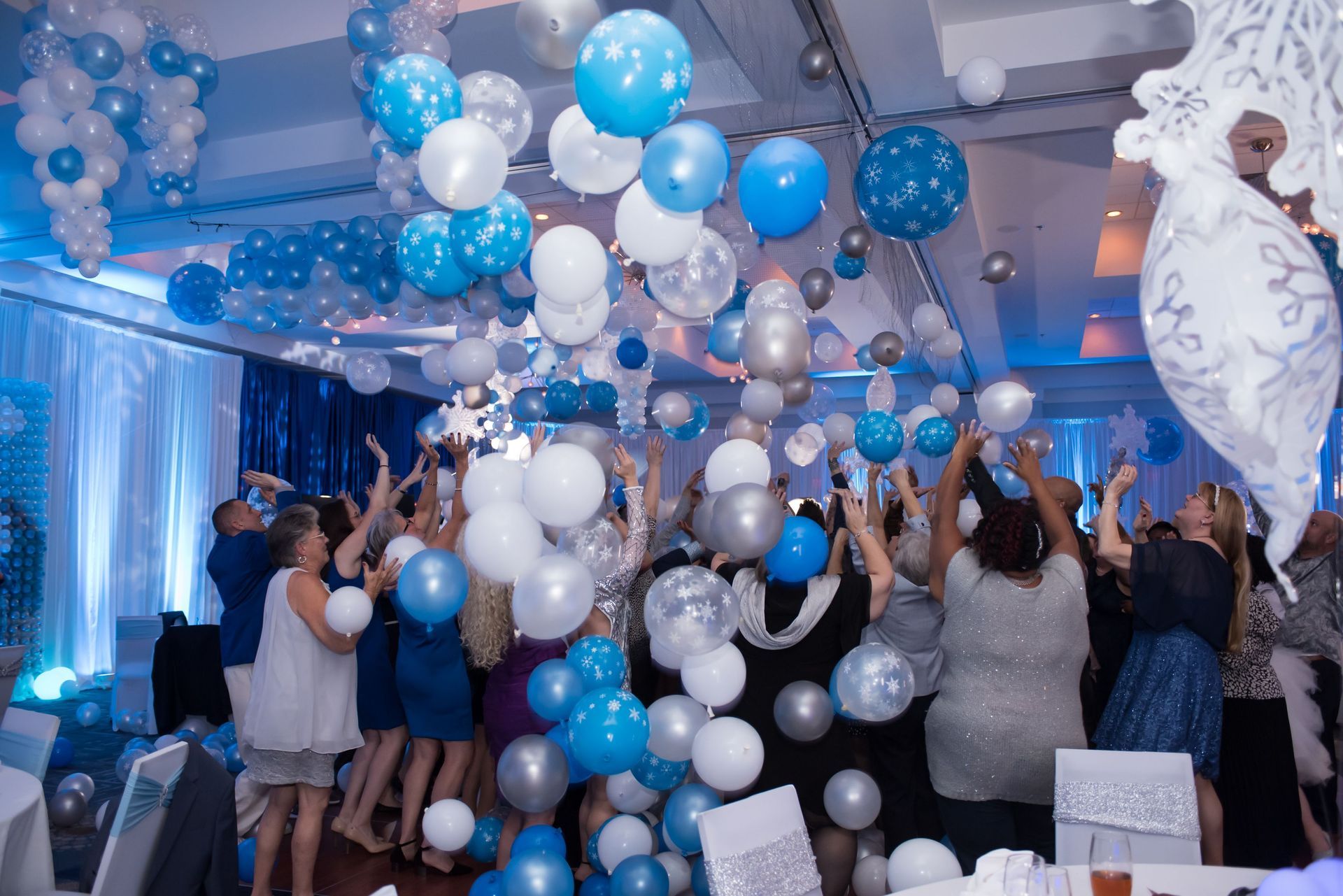 A group of people are dancing in a room filled with balloons. Balloon Drop