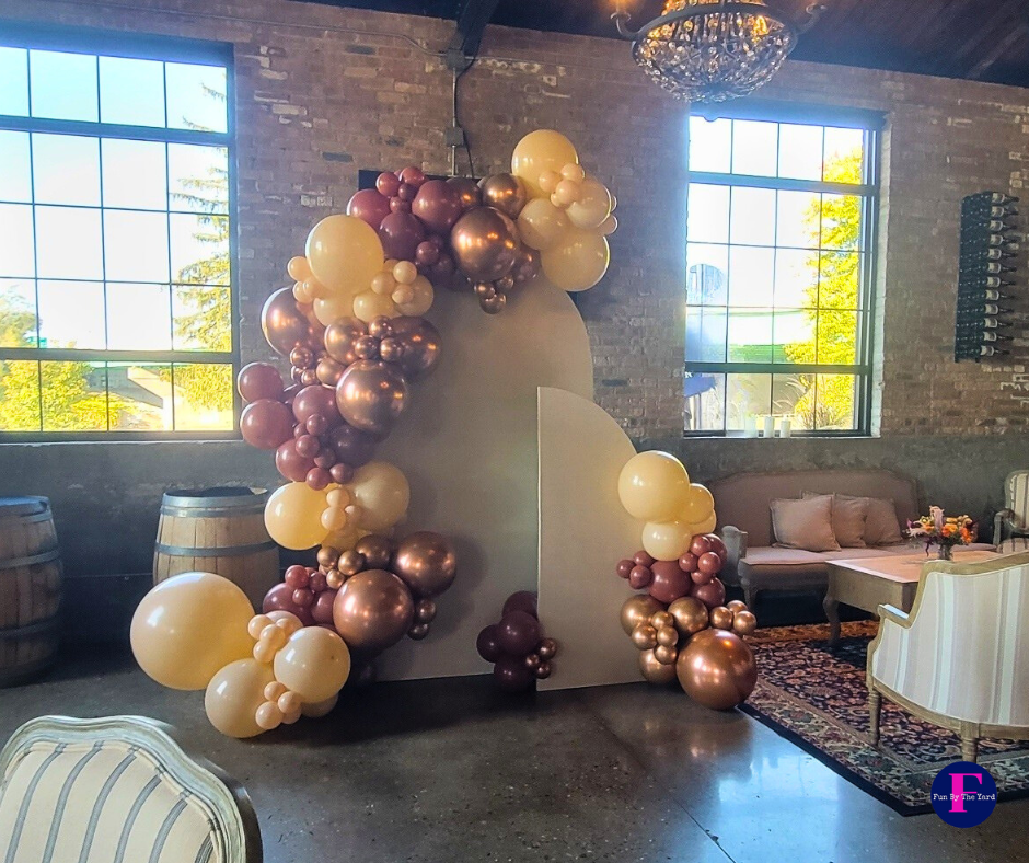 Balloons in shades of gold and brown decorate a wall. The setting is an event space with windows and exposed brick.