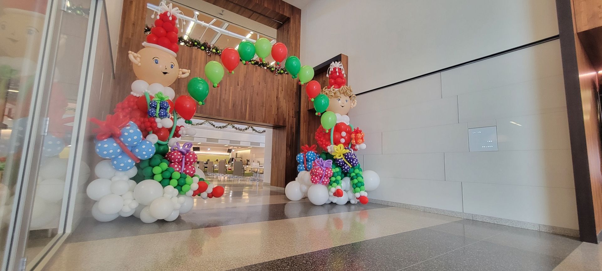Christmas balloon elf decorations arching over a doorway in a shopping mall.