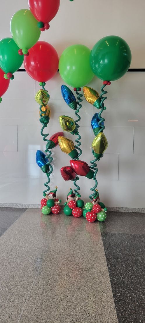 Christmas-themed balloon display: red, green, and gold balloons shaped like lights, on a gray speckled floor.