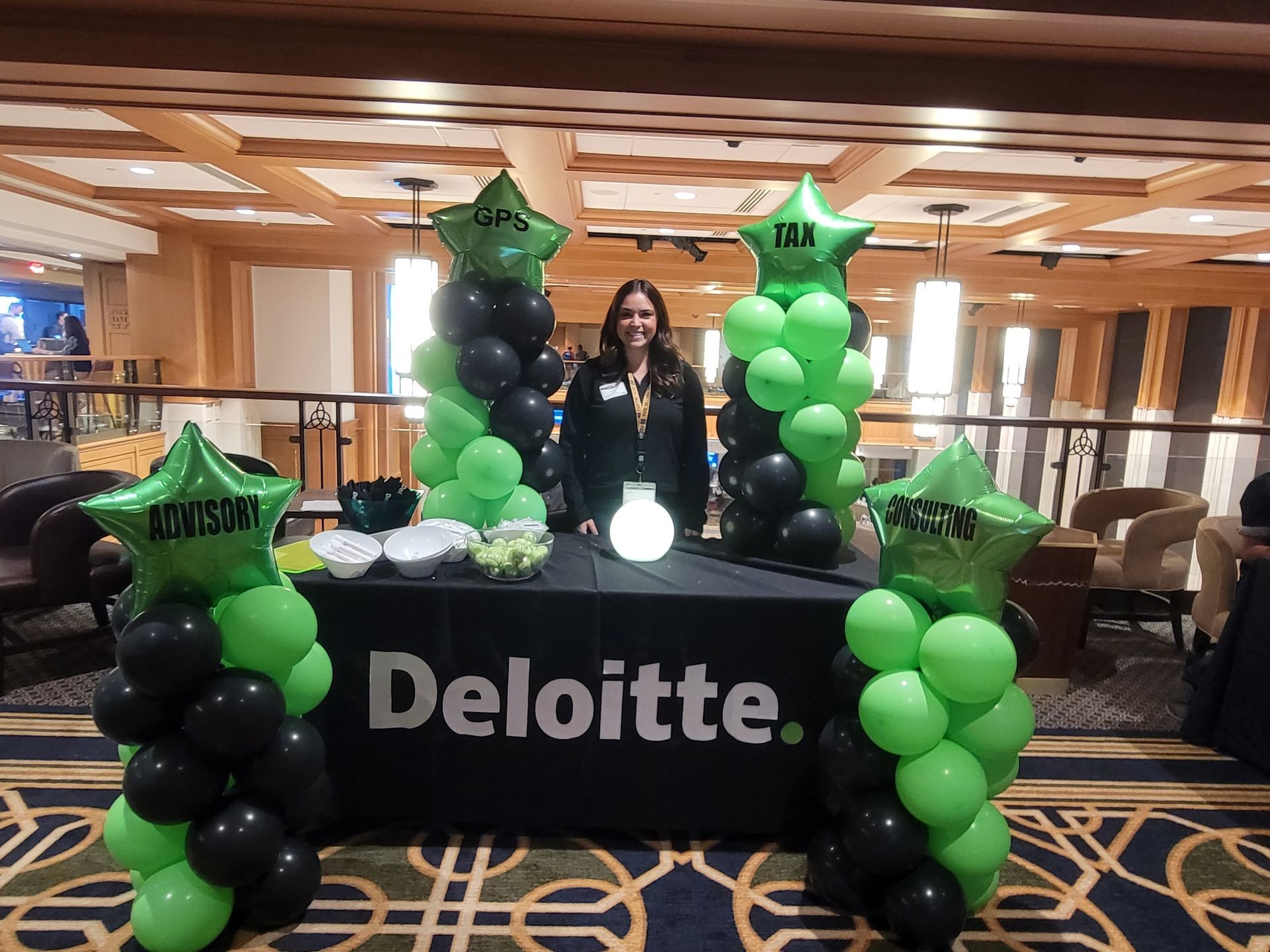 A woman is standing in front of a table decorated with green and black balloons.
