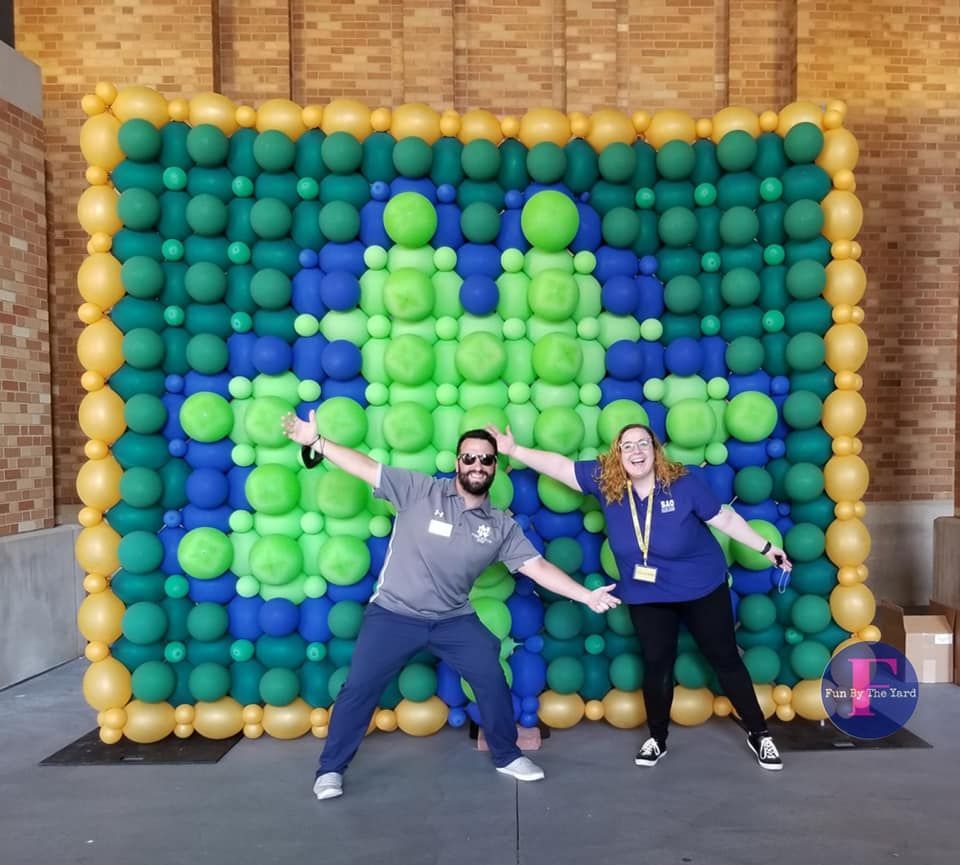 a man and a woman are posing in front of a wall made of balloons shaped like a shamrock