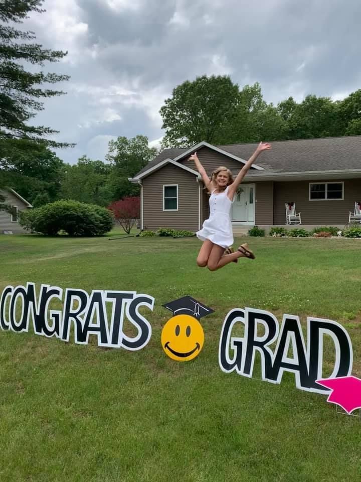 A woman is jumping in the air in front of a congratulations grad sign.