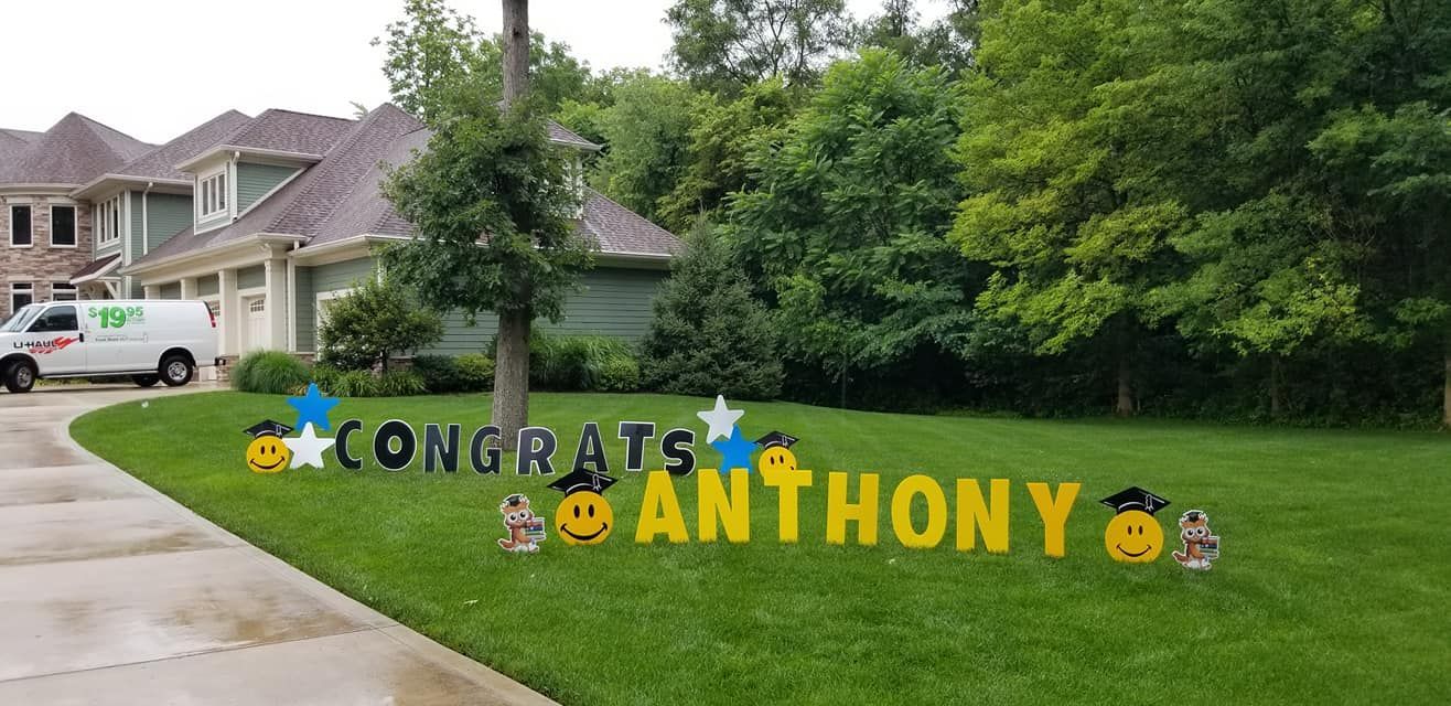 A congratulations sign for anthony is in the grass in front of a house.