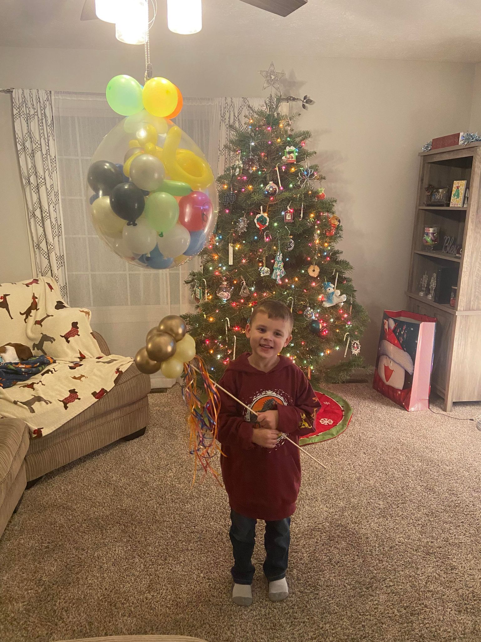 A young boy is holding a balloon in front of a christmas tree.