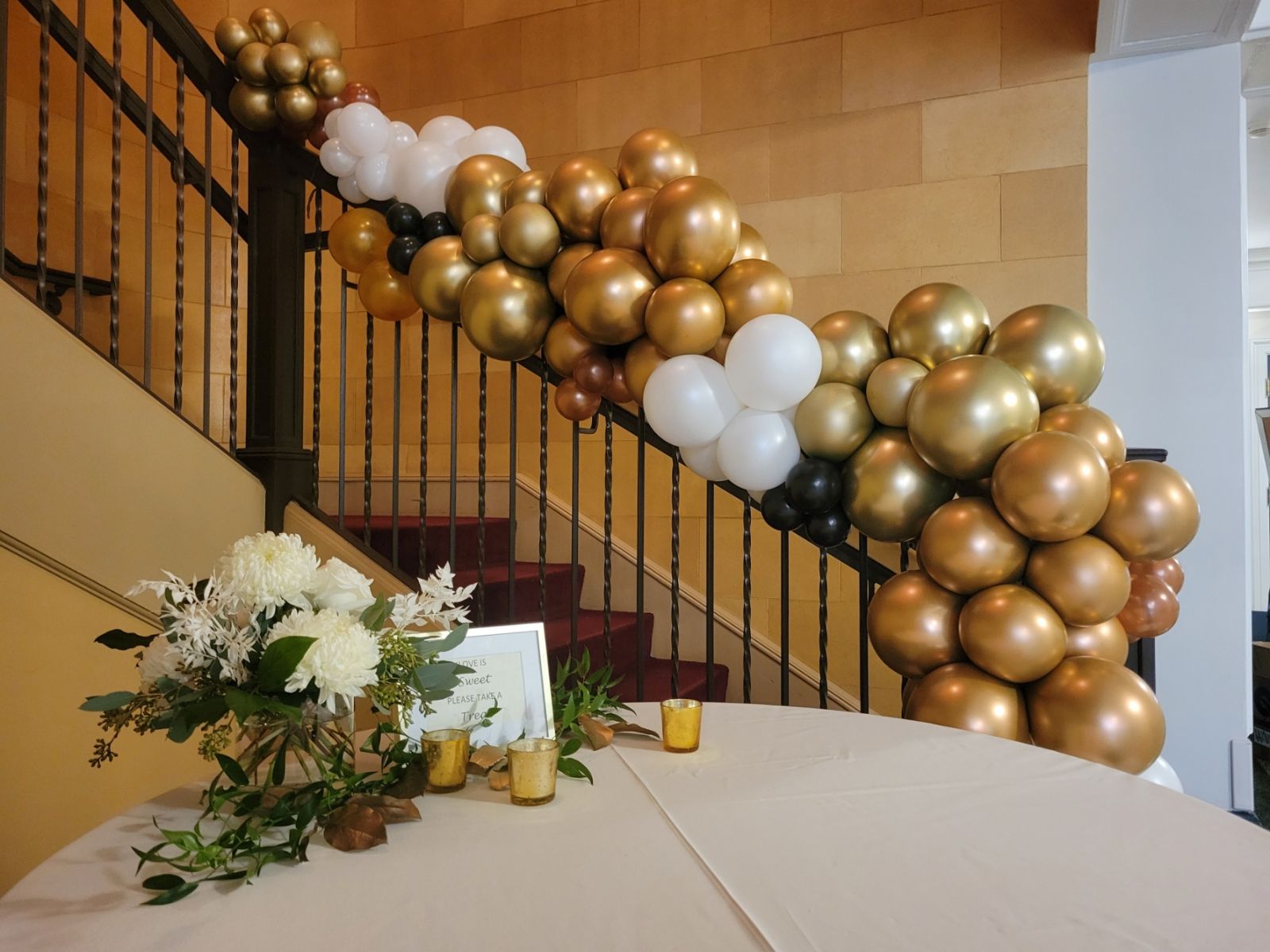 A balloon garland of gold and white cascading down a stair railing for a wedding