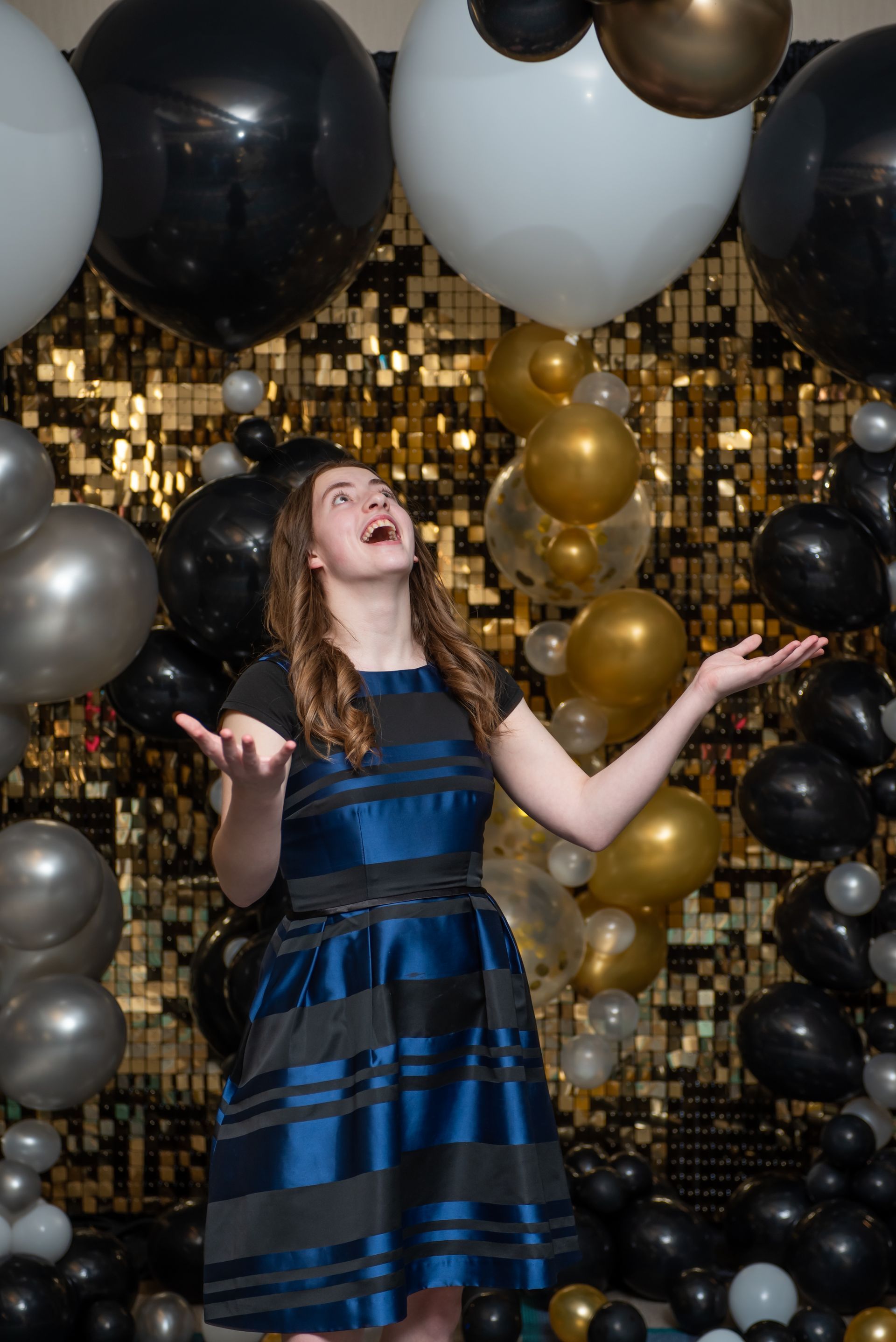 A woman in a blue dress is standing in front of a wall of balloons.