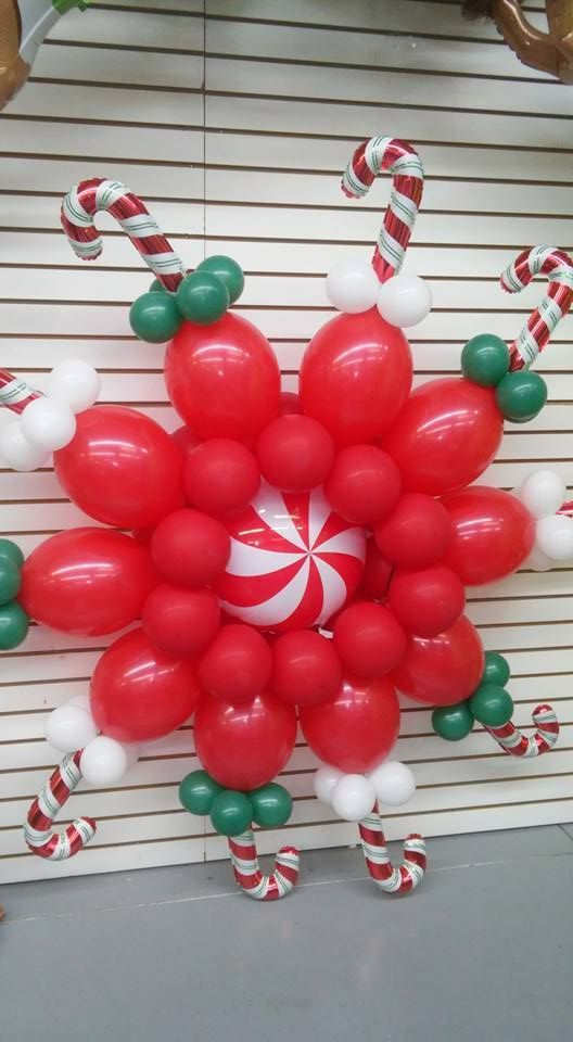 Red, white, and green balloon snowflake decoration with candy cane arms, on a white slat wall.