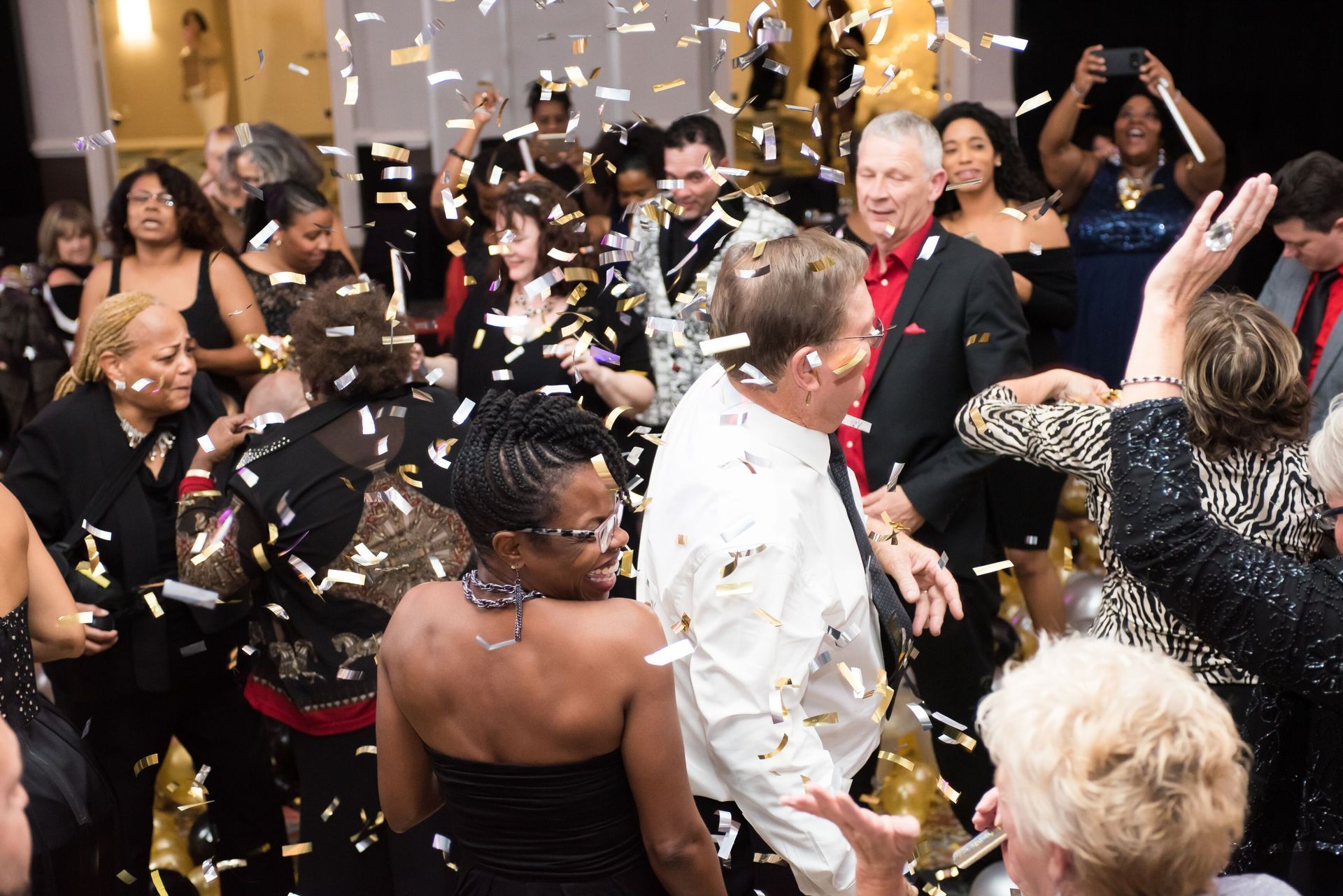 A crowd of people are dancing in a room with confetti falling.  Balloon Drop