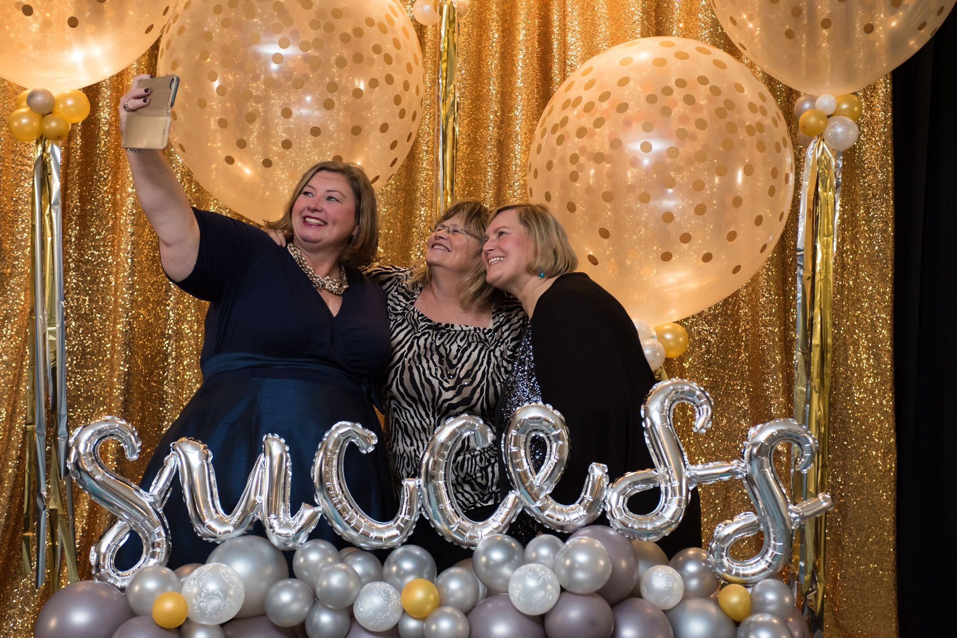 Three women are taking a selfie in front of balloons.