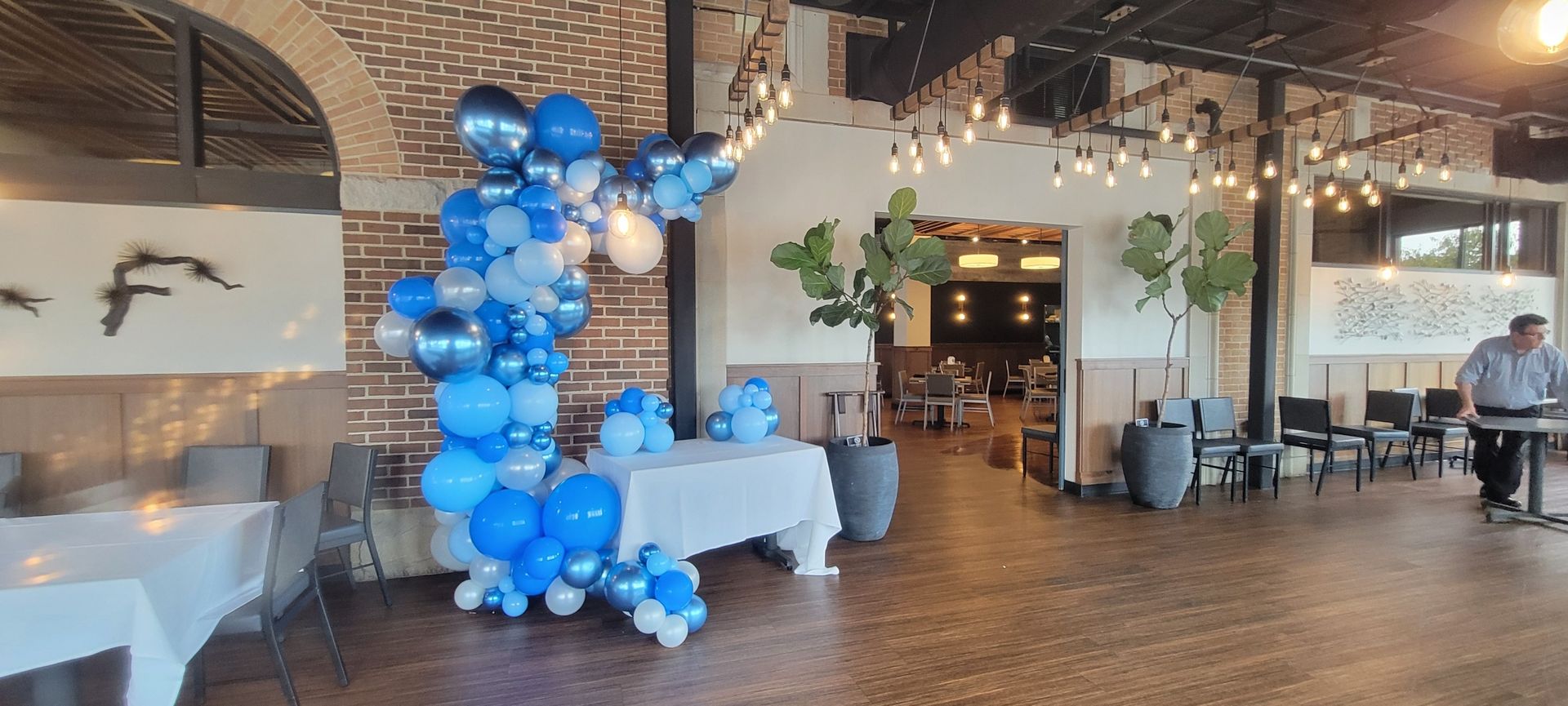 A decorated venue with blue balloons, tables, and plants, likely for a celebration.