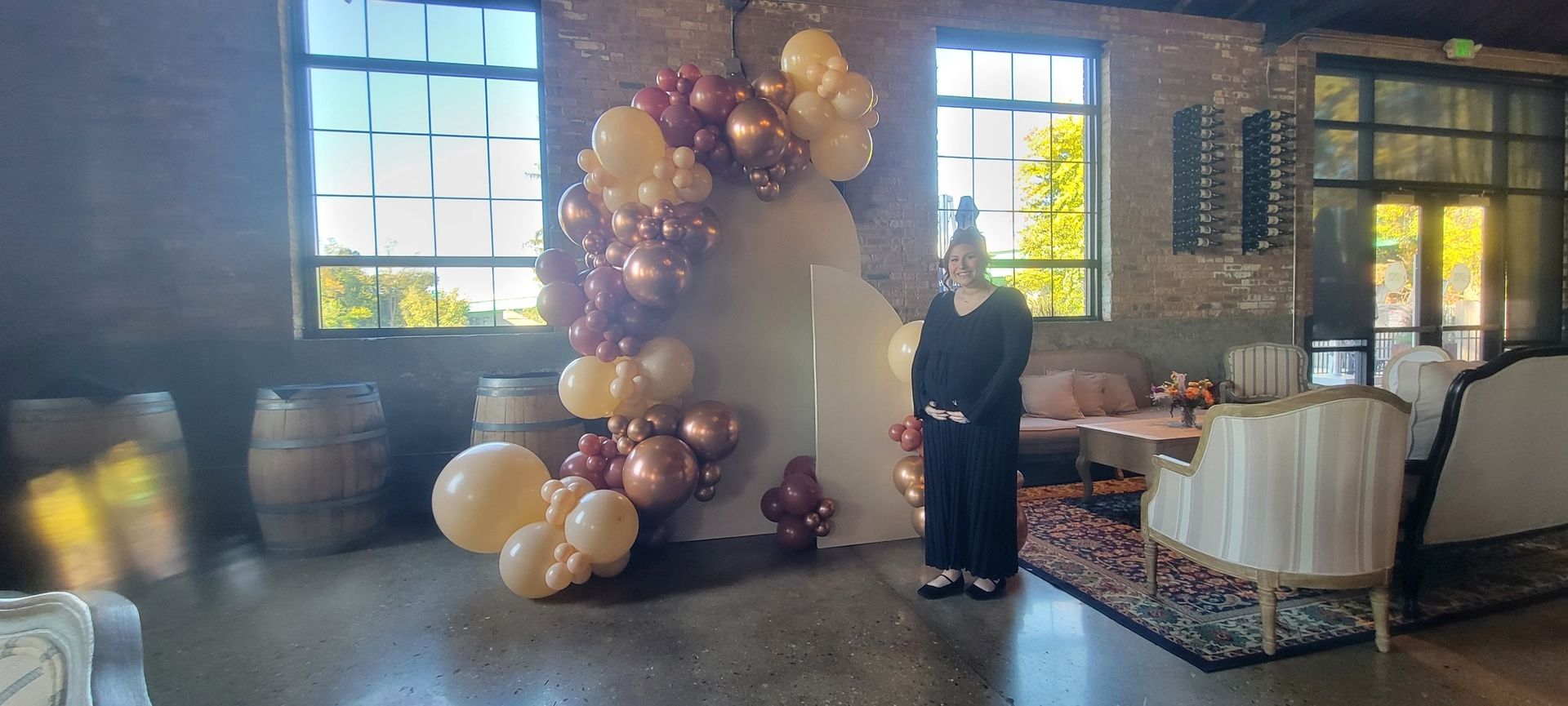 Woman stands in front of a white arch decorated with balloons, party setting.