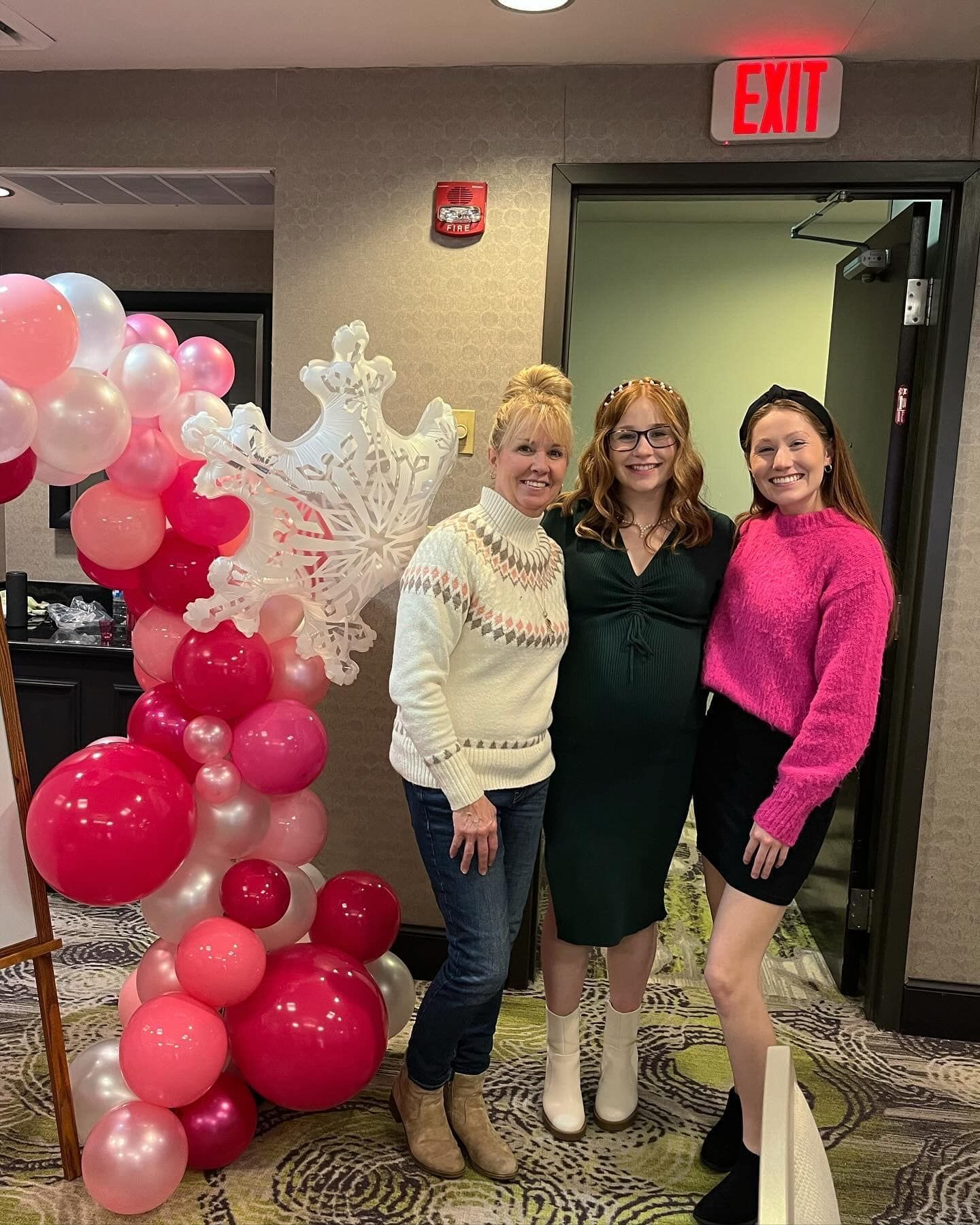 Three women pose together near a balloon arch at an event.