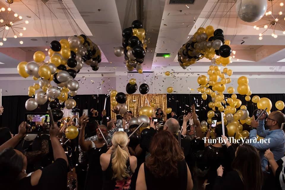 A crowd of people are gathered in a room with balloons and confetti.  Balloon Drop