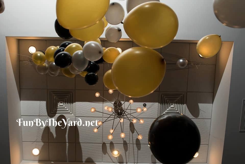 A bunch of yellow and black balloons hanging from the ceiling.  Balloon drop