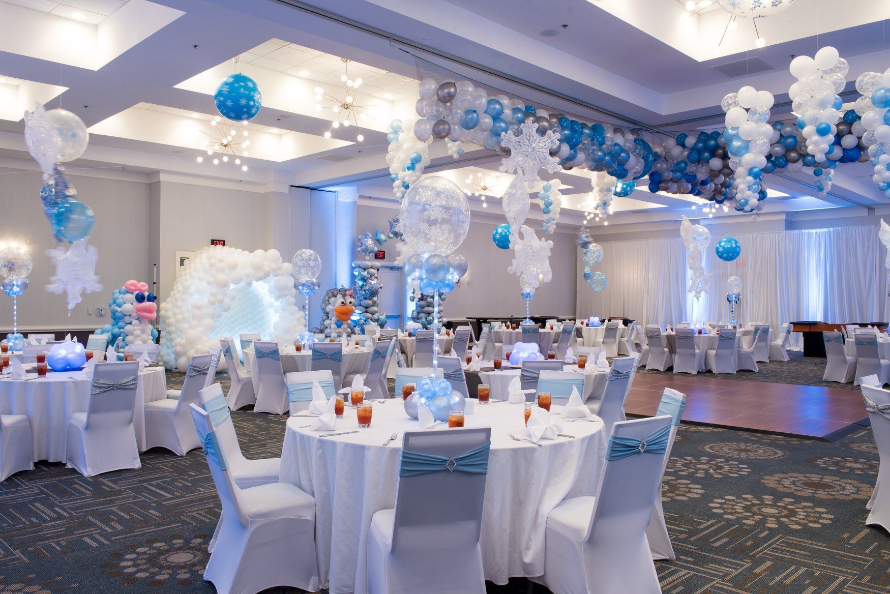 A large room filled with tables and chairs and balloons.  Christmas winter wonderland themed party