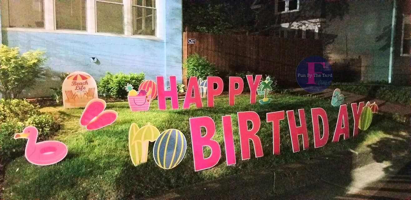 A happy birthday sign is sitting in the grass in front of a house.  Beach themed yard card.