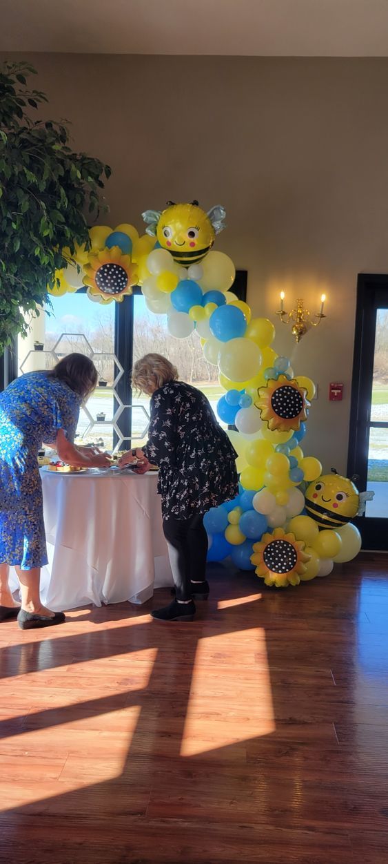Two women are standing in front of a table decorated with balloons.