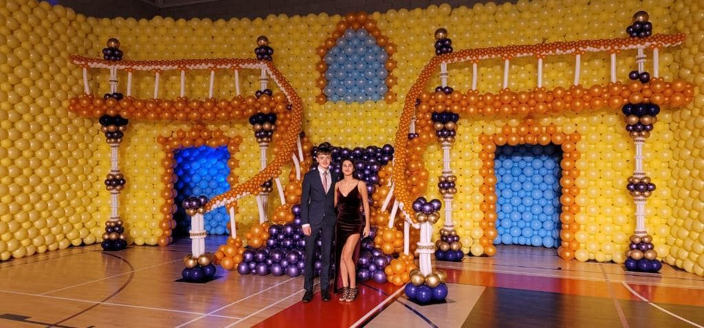 A man and a woman are standing in front of a wall of balloons.