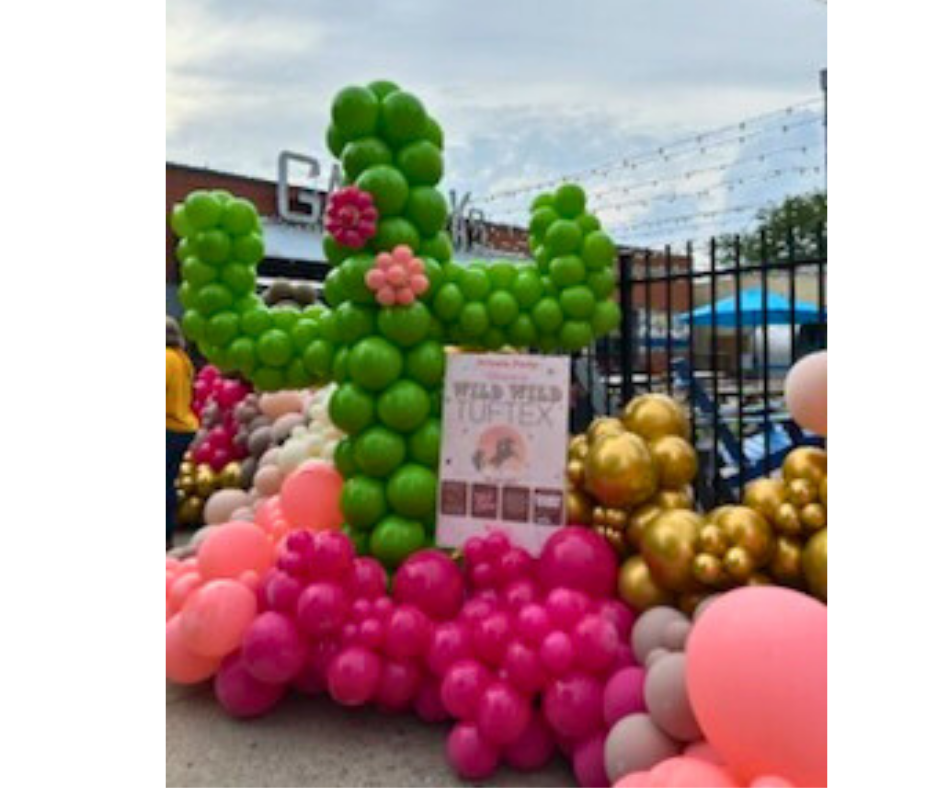 A large green balloon cactus with pink and gold balloon decorations; sign for 