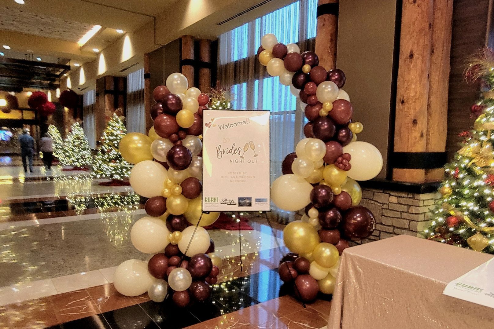 A balloon arch with a sign, decorated for Christmas in a hotel lobby.