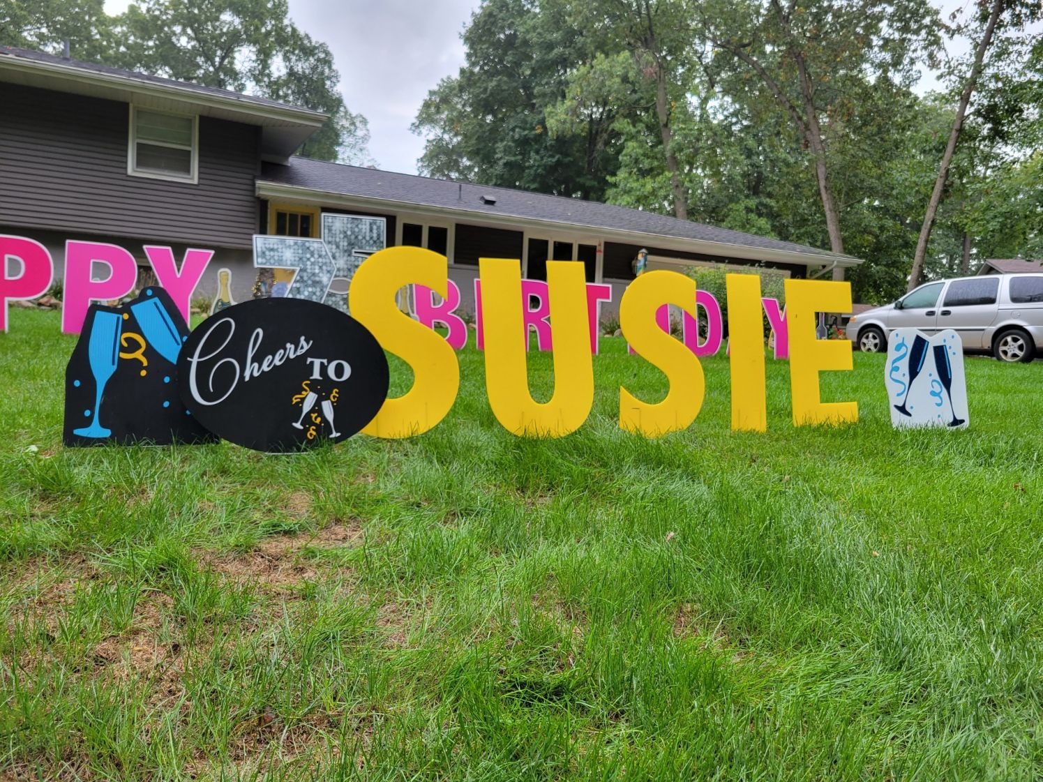 A yard sign that says happy cheers to susie is in front of a house.