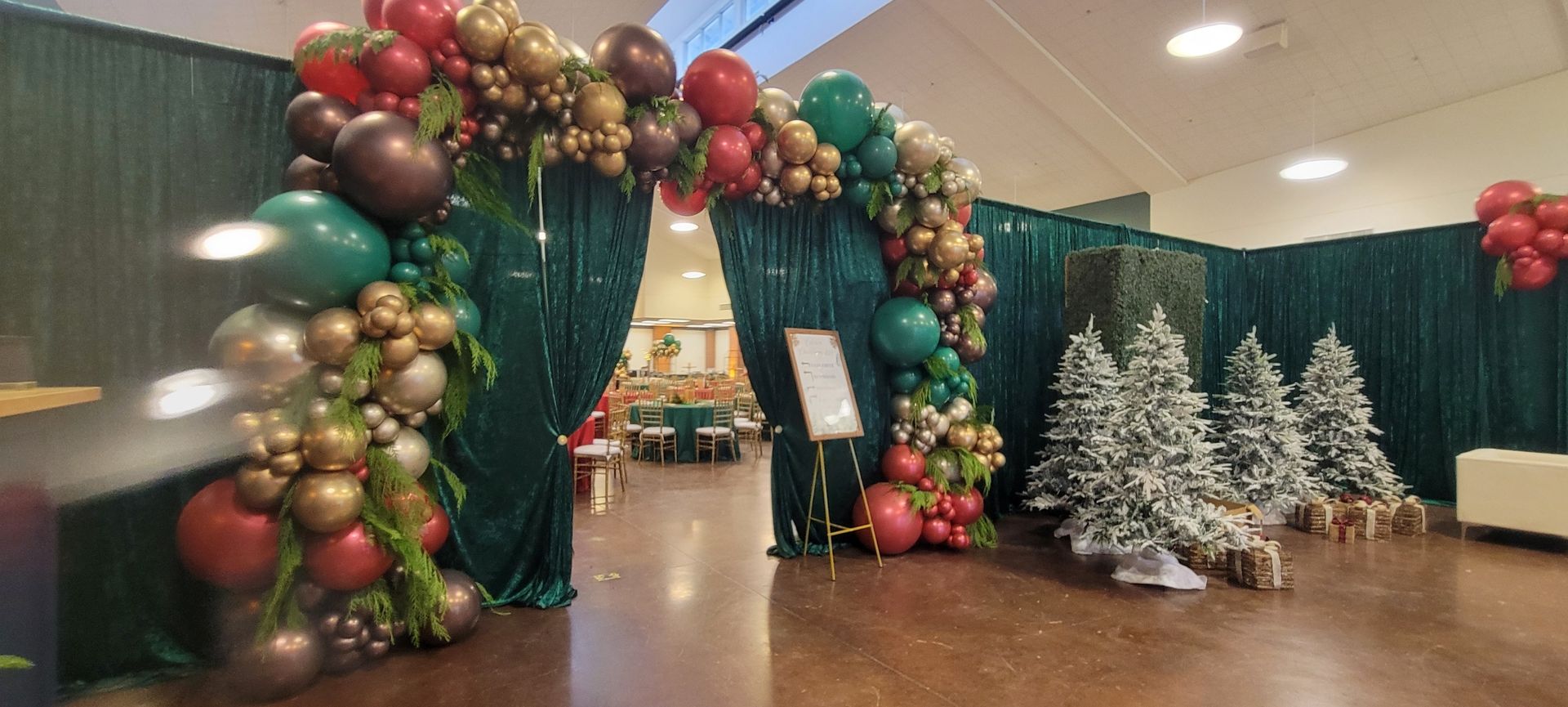 A festive indoor archway decorated with balloons and Christmas trees.
