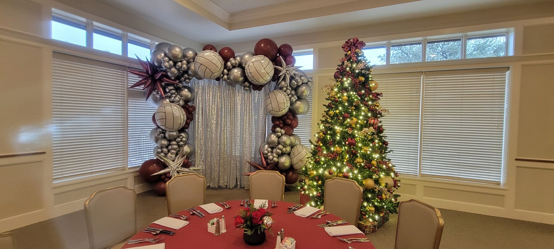 Festive dining room with a decorated Christmas tree, balloon arch, and red tablecloth.